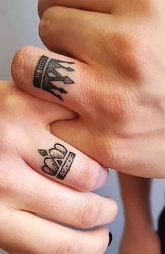 two people holding hands with tattoos on their fingers and one has a crown tattooed on it