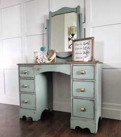 an antique blue desk with drawers and a mirror on the top, in front of a white paneled wall