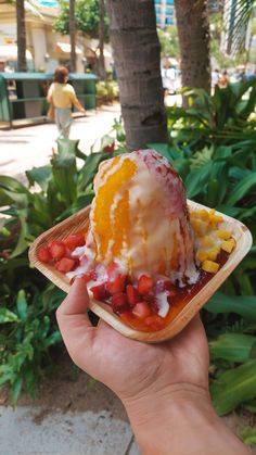 someone is holding up an ice cream cone with fruit on it in front of some trees