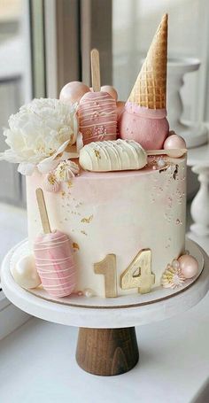 a birthday cake decorated with pink and gold decorations on a table next to a window