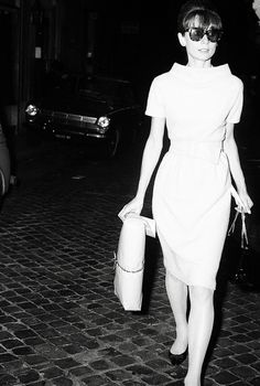 black and white photograph of woman walking down the street at night with her purse in hand