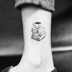 a black and white photo of a woman's foot with a coffee cup on top of books