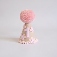 a pink and white birthday hat with pom - poms on the top is shown