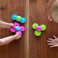 two children playing with toys on a wooden table, one is holding the other's hand