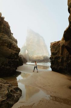 a person walking on the beach in front of some rocks and water with a large rock formation behind them