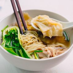 a bowl filled with noodles, meat and veggies next to chopsticks