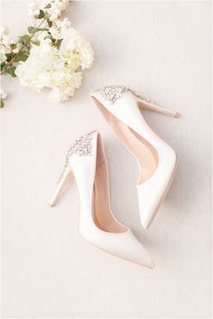 two pairs of white high heeled shoes next to flowers