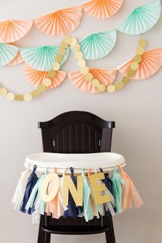 a baby's first birthday party with paper fan garlands and one sign on the chair