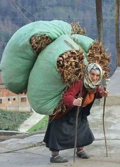 a woman walking down the street with a large bag on her head and a stick in her hand