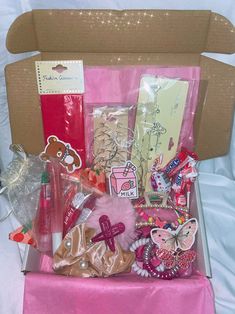 an open cardboard box filled with lots of different types of candy and candies on a pink table cloth