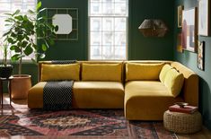 a living room with green walls and yellow couches in the corner, potted plants on either side