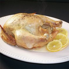 a whole chicken on a white plate with lemons