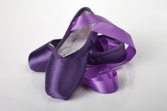 two purple ballet shoes tied together on a white surface with one shoe in the middle