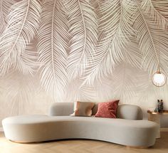 a white couch sitting on top of a wooden floor next to a wall covered in palm leaves