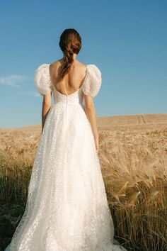 a woman in a white dress standing in a wheat field with her back to the camera