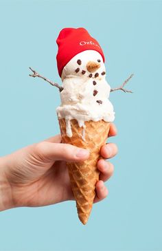 a hand holding an ice cream cone with a snowman on top and a red hat