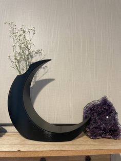 a vase with some flowers and rocks on a wooden shelf next to a wall mounted clock