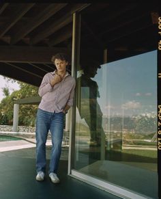 a man leaning against a glass door with his hand on his chin and looking at the camera