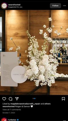 a vase filled with white flowers sitting on top of a wooden counter next to a menu