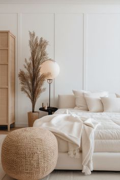 a white bed sitting in a bedroom next to a tall lamp and a wooden dresser