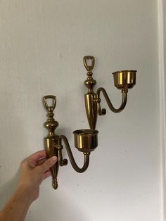 a person is holding two brass candle holders on the wall with one light turned on