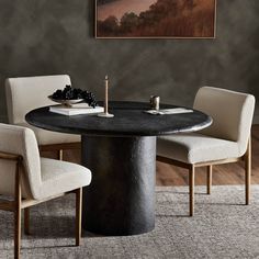 a round table with chairs around it and a painting hanging on the wall behind it