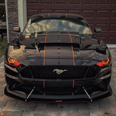 the front end of a black sports car with orange stripes on it's hood