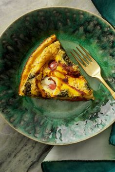 a piece of quiche on a green plate with a fork and napkin next to it