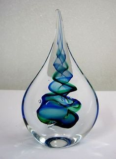 a blue and green glass vase sitting on top of a white table next to a wall