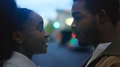 a man and woman standing next to each other in the street looking at each other