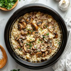 an overhead view of rice with mushrooms and parsley in a black bowl on a white table