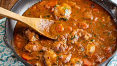 a skillet filled with meat and vegetables on top of a blue towel next to a wooden spoon