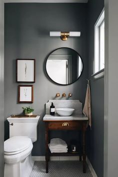 a white toilet sitting next to a bathroom sink under a round mirror on a wall