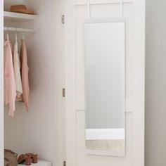 a white closet with clothes hanging on hooks and a mirror over the door in front of it