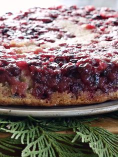 a cake with berries on it sitting on top of a metal platter next to pine branches