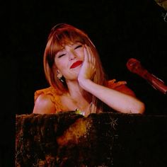 a woman sitting at a podium with her hand on her face while holding a microphone