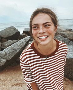 a young woman standing on top of a sandy beach next to the ocean and rocks