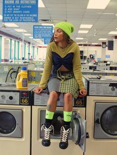 a woman sitting on top of a stack of washers in a laundroom