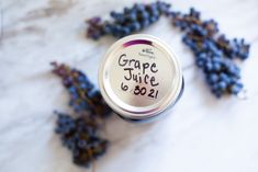 grape juice in a tin next to some purple grapes on a table with the words grape juice printed on it