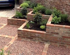 a car is parked in front of a brick wall and garden bed with plants growing out of it