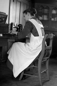 a woman in an apron is sitting at a sewing machine