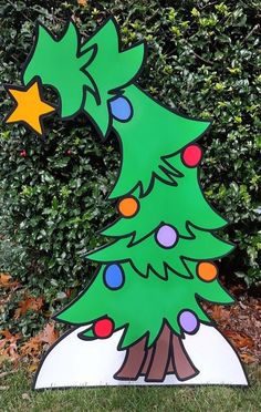 a wooden christmas tree with lights on it in front of some bushes and shrubbery