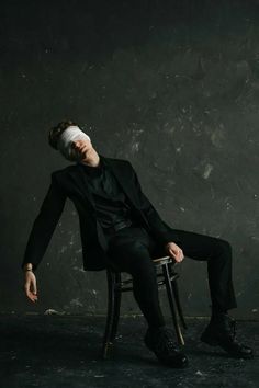 a man in a suit and blindfold sitting on a chair with his eyes closed