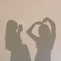 two women standing next to each other in front of a white wall with the shadow of their hands