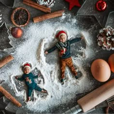 two small children laying in the snow next to christmas decorations and baking utensils