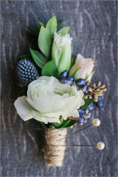 a bouquet of flowers sitting on top of a gray table next to blue berries and greenery