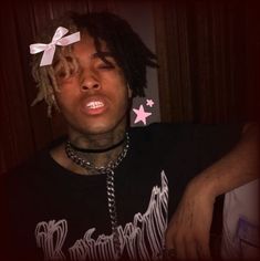 a young man with dreadlocks and a pink bow on his head is staring at the camera