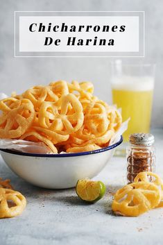 a white bowl filled with cheetos next to a glass of orange juice and lime