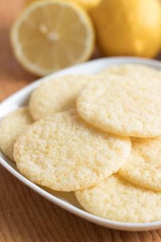 a white plate topped with lemon cookies next to sliced lemons on a wooden table