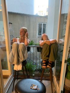 two people sitting on chairs in front of a window looking out at the balcony area